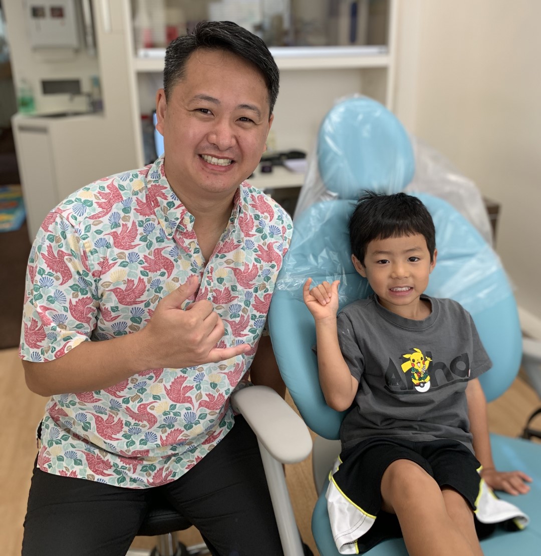 Dentist and young boy patient both making shaka signs while sitting in dental chair